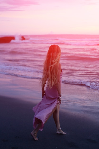 A woman in a dress goes to the sea at sunset