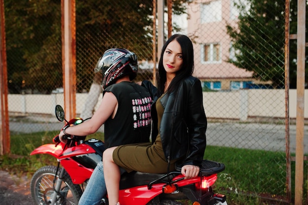 Woman in dress and leather jacket riding a motorbike with another man