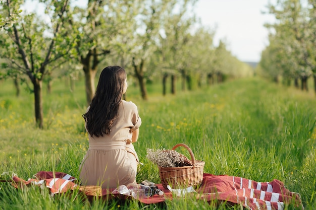 Woman in dress sitting at summer picnic at nature with wine