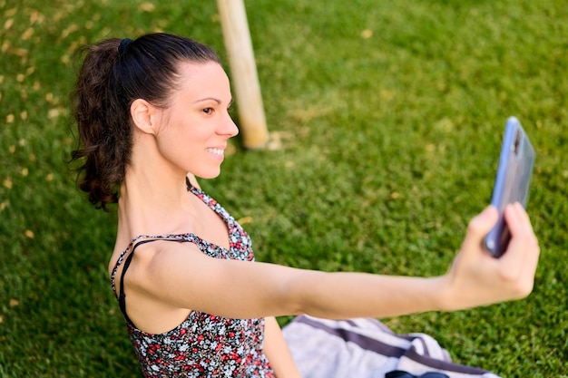 Donna in vestito sorridente che prende un selfie sull'erba