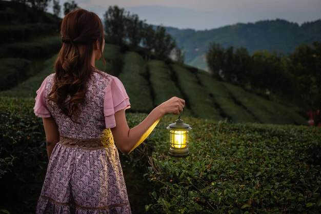 Photo woman in a dress stands holding a lantern lit by warm yellow lights in the forest at dusk copy space background