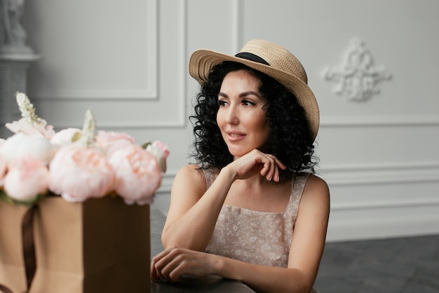 Woman in a dress and a straw hat next to a bouquet of flowers