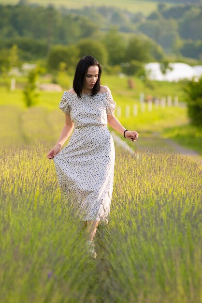 Женщина в платье идет по полю с высокой травой.