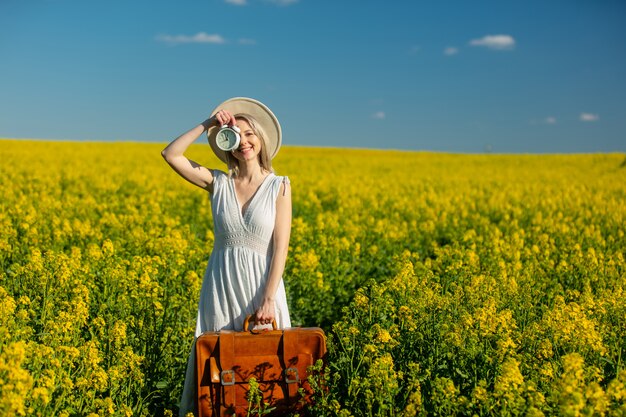 Woman in dress with suitcase and alarm clock in rapeseed field