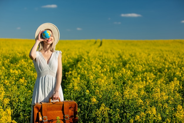 Woman in dress with suitcase and Earth globe in rapeseed field