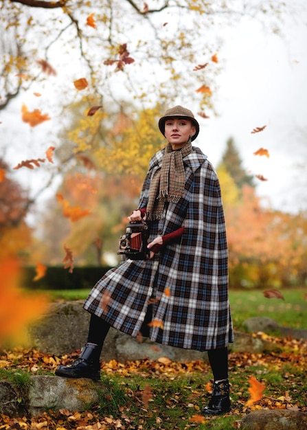 A woman dressed as Sherlock Holmes with vintage camera looking for evidence in autumn park