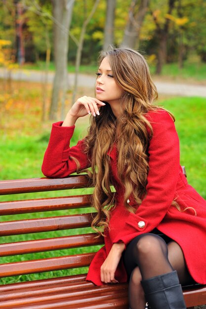 Donna vestita di cappotto rosso seduto nel parco d'autunno.