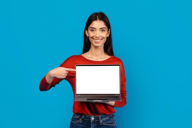 Photo a woman dressed in a red sweater is holding a laptop with white blank screen in her hands isolated