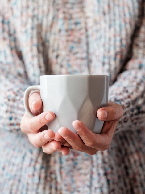 Photo a woman dressed in a wool sweater on a cold day and holding a cup of warm tea in her hands