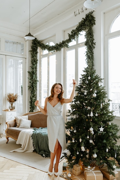 A woman dresses up a Christmas tree at home in a beautifully decorated living room.