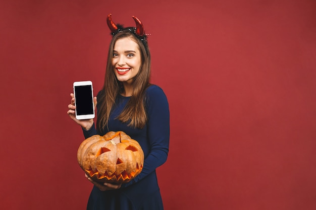 Женщина, одетая в черный дьявол Хеллоуин костюм с оголовьем ведьмы для тематической вечеринки. Она держит тыкву для «трюк или угощение»