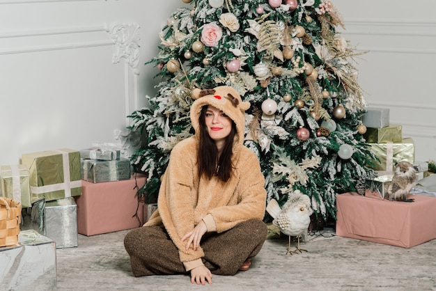 Woman dressing Christmas tree, smiling, sitting in a new year interior