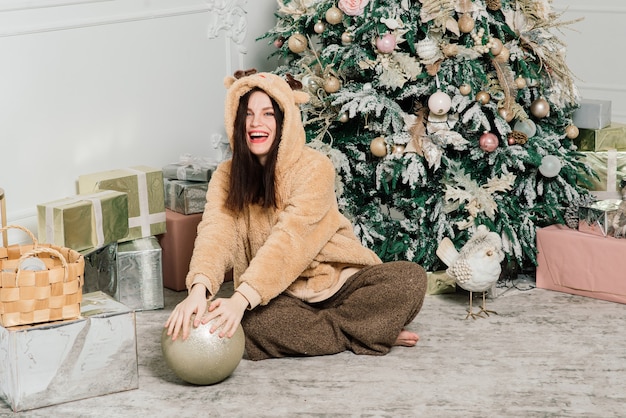 Woman dressing Christmas tree, smiling, sitting in a new year interior