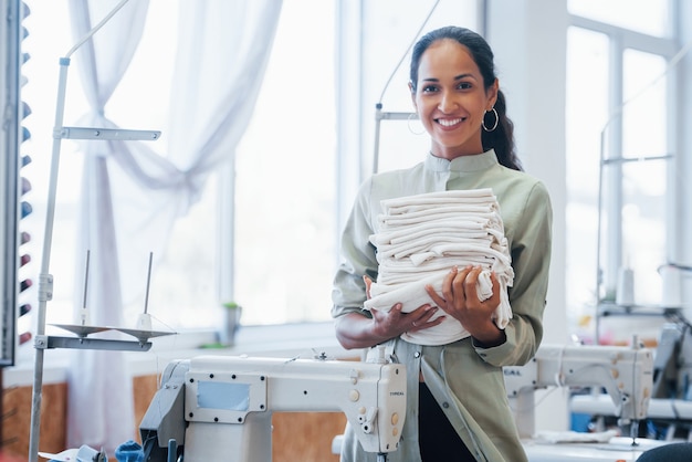 Woman dressmaker stands in the factory with cloth in hands.