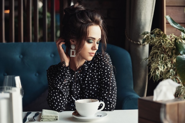 女性はレストランやカフェのテーブルでコーヒーを飲む