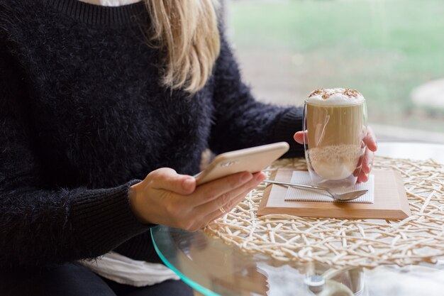 Woman drink Hot latte or Cappuccino coffee in cafe using mobile phone in hand. Coffee break.