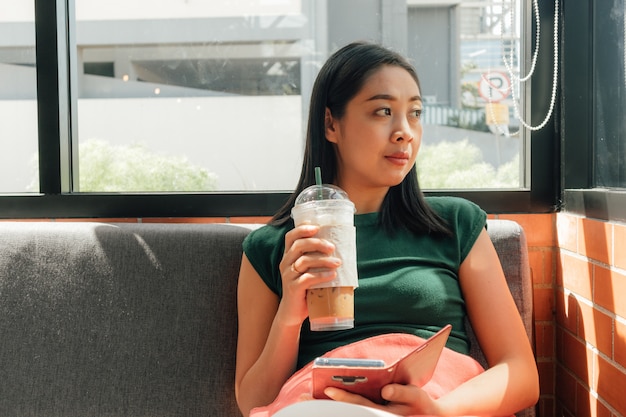 Woman drink iced coffee and use her smartphone 