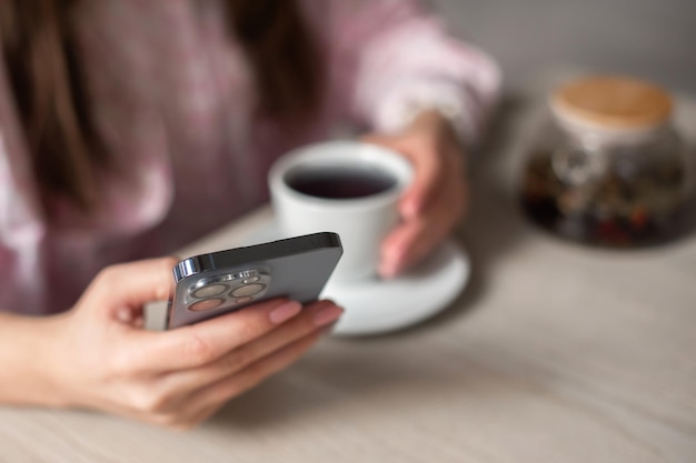 Woman drink tea searching for information in phone shallow depth of field photo