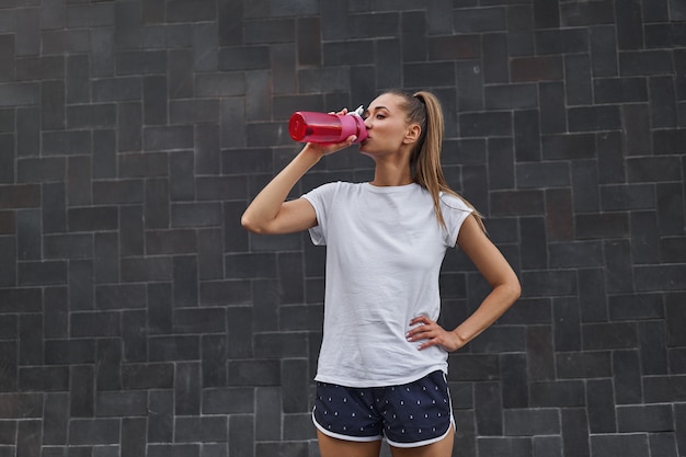 女性は朝のトレーニングの後に水赤いボトルを飲みます