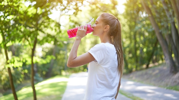 女性は朝のトレーニングの後に水赤いボトルを飲みます。