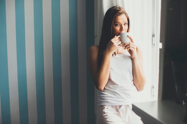 Женщина пьет кофе у окна в дневное время