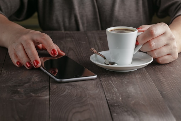 Woman drinking coffee in cafe and looking at the phone screen