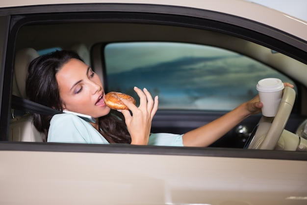 Woman drinking coffee and eating donnut on phone