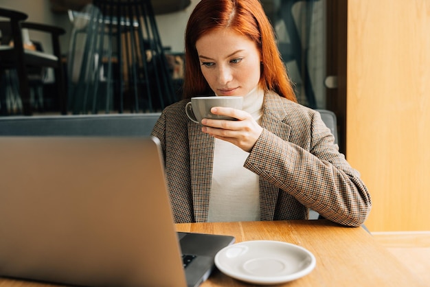 Woman drinking coffee and looking at laptop while sitting at a table in cafex9xA