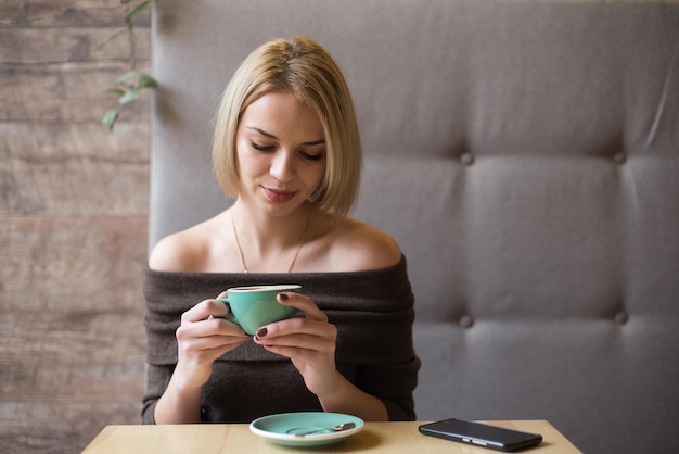 Женщина пьет кофе по утрам в ресторане Мягкий фокус на глазах Селлфон на столе