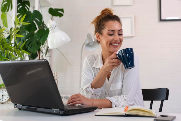 Woman drinking coffee in morning and using laptop for work