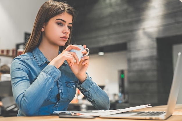 The woman drinking a coffee near the modern laptop