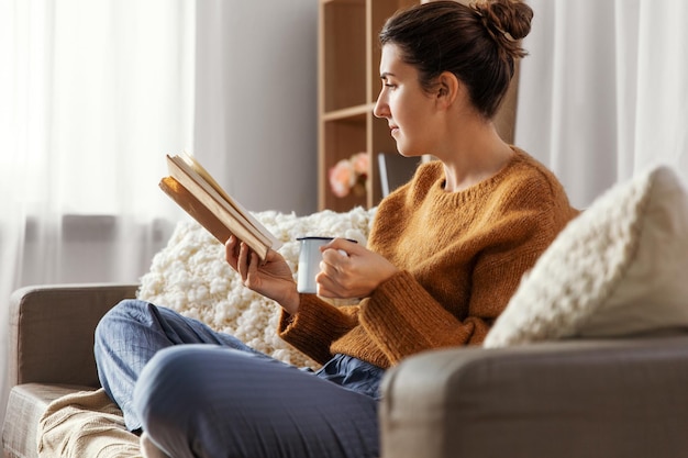 Женщина пьет кофе и читает книгу дома.