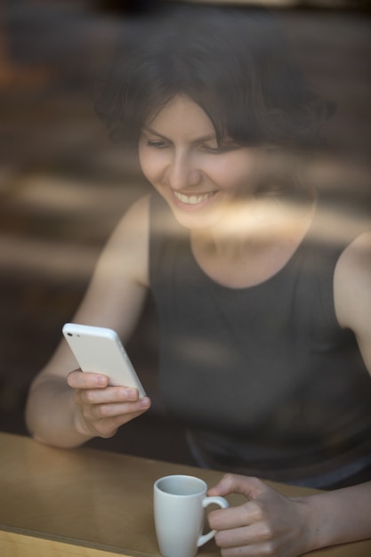 Photo woman drinking coffee and smiling while looking mobile