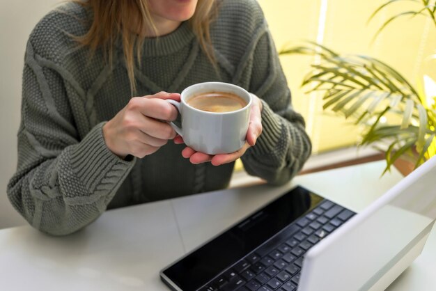 コーヒーを飲みながらデジタルタブレットのノートパソコンを使う女性