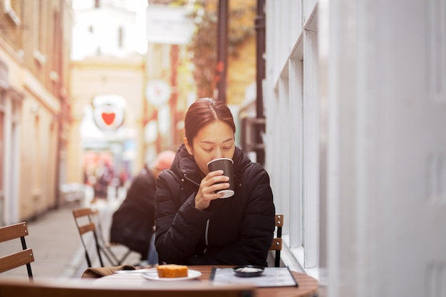 Photo woman drinking coffee while sitting in sidewalk cafe