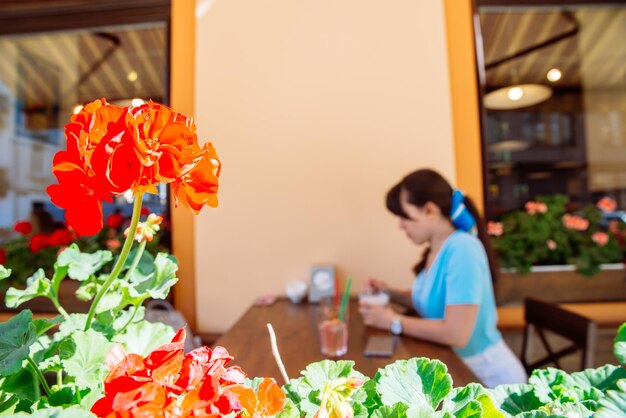カフェで冷たい飲み物を飲む女性は、ぼやけた背景の前の花に焦点を当てる