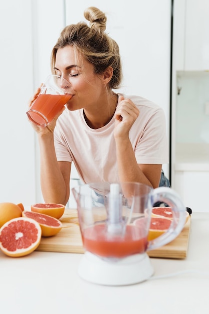 白いキッチンで絞りたての自家製グレープフルーツジュースを飲む女性