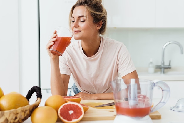 白いキッチンで絞りたての自家製グレープフルーツジュースを飲む女性