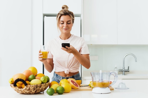 Woman drinking freshly squeezed homemade orange juice and taking photos by her smartphone