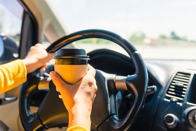 車の中で、車を運転中にホットコーヒーテイクアウトカップを飲む女性