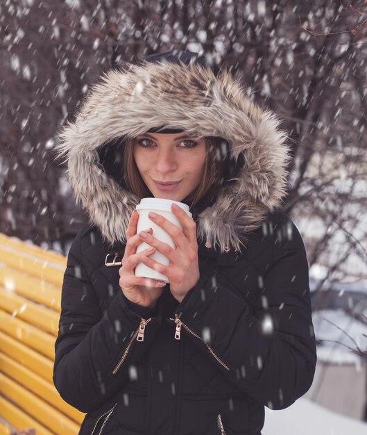 Woman drinking hot coffee or tea from mug under snowflakes in winter