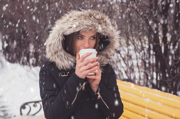 Woman drinking hot coffee or tea from mug under snowflakes in winter