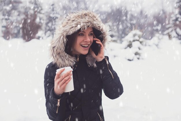 冬の雪片の下でマグカップからホットコーヒーやお茶を飲む女性