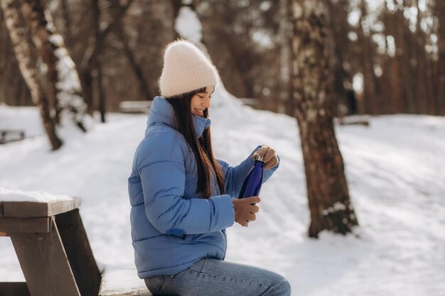 Woman drinking hot tea holding vacuum flask in winter park