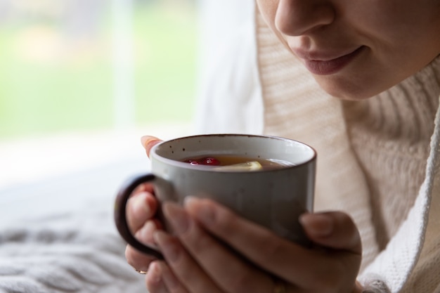 窓際の秋の時間インフルエンザの季節に座って朝に家で休んでいる間熱いお茶を飲む女性