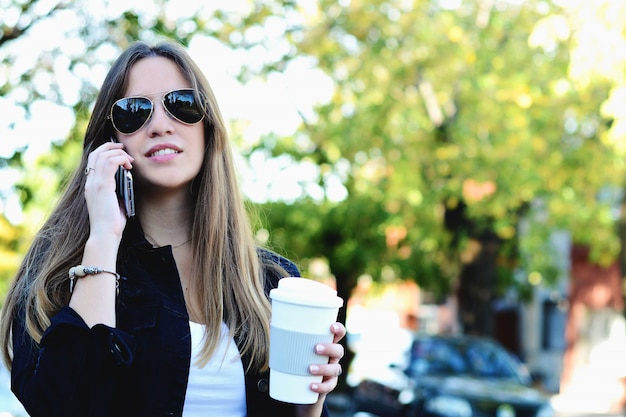 Woman drinking paper cup of coffee and using a her phone