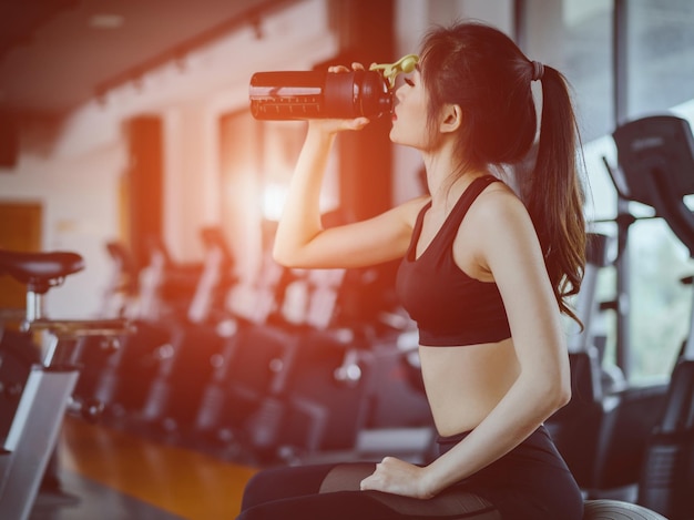 Photo woman drinking protein from bottle in gym