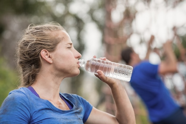 Woman drinking water from bottle during obstacle course in boot camp