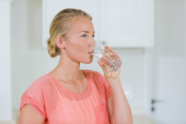 Женщина пьет воду из стекла на кухне