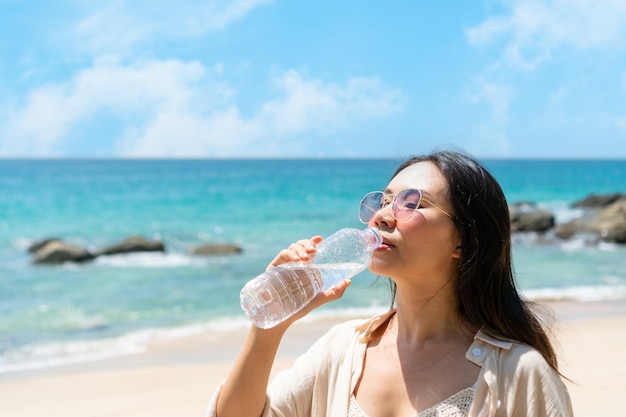 海沿いの夏の日差しの中でペットボトルから水を飲む女性健康と新鮮さの概念喉の渇きの水の浄化クローズアップコピースペース